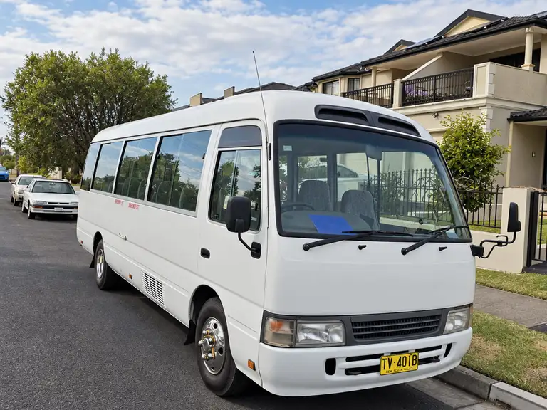 White Toyota Coaster minibus on a street.